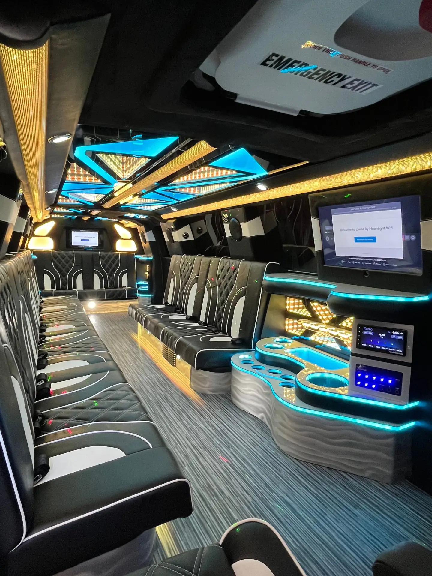 Interior of Basking Ridge Limousine’s 2025 GMC Yukon Stretch featuring plush black and white leather seating, golden and blue LED ceiling lights, and a custom bar area.