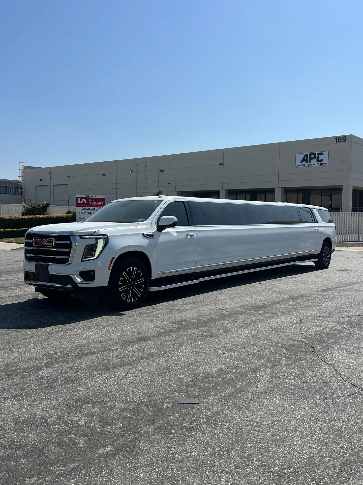 Basking Ridge Limousine’s white 2025 GMC Yukon Stretch Limousine parked in front of an industrial building under a clear blue sky.