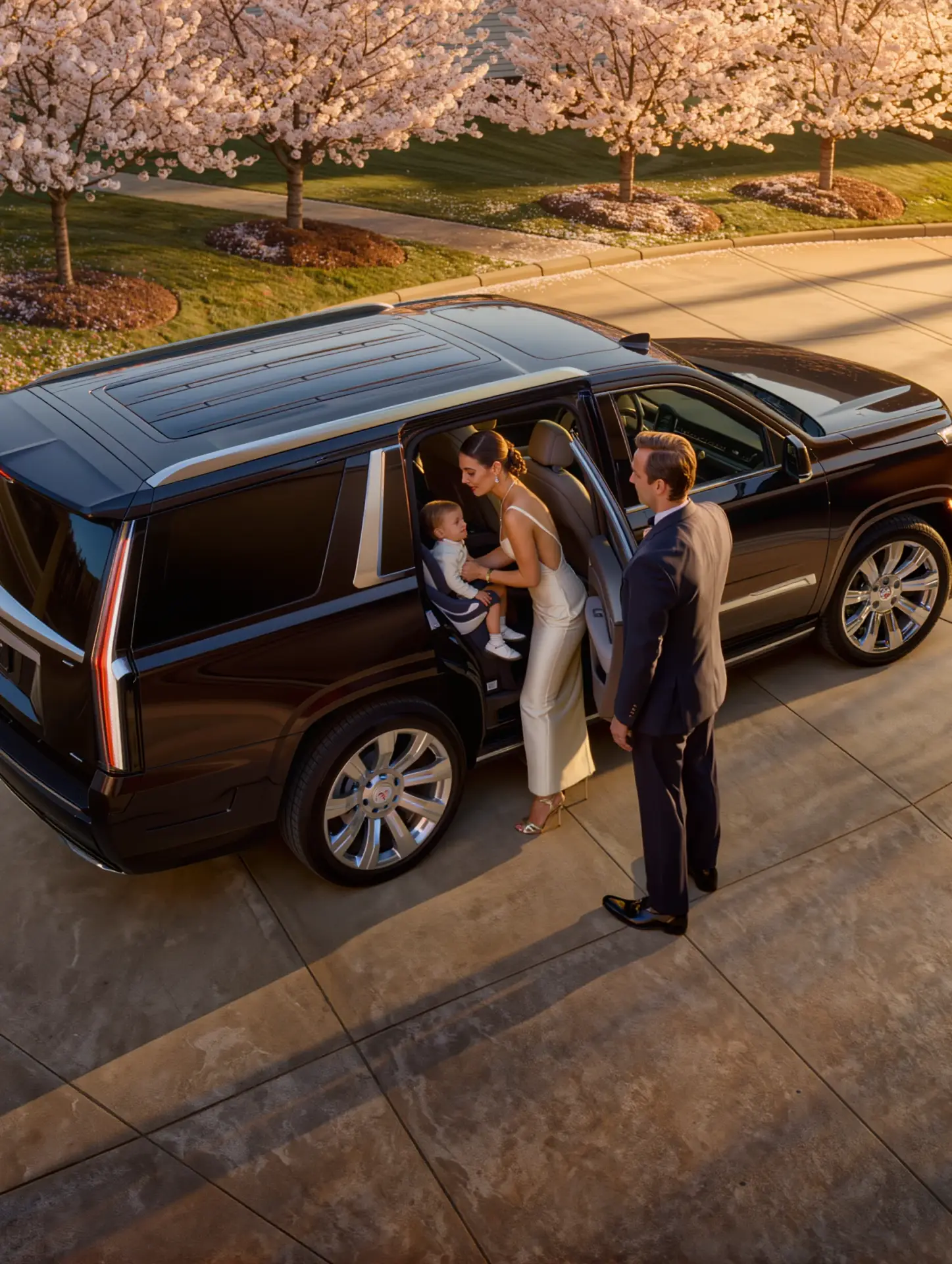 Elegantly dressed mother helping young child into rear passenger seat of luxury black Cadillac Escalade SUV with child safety seat installed professional chauffeur holding rear door open New Jersey suburban neighborhood Basking Ridge Limousine Services