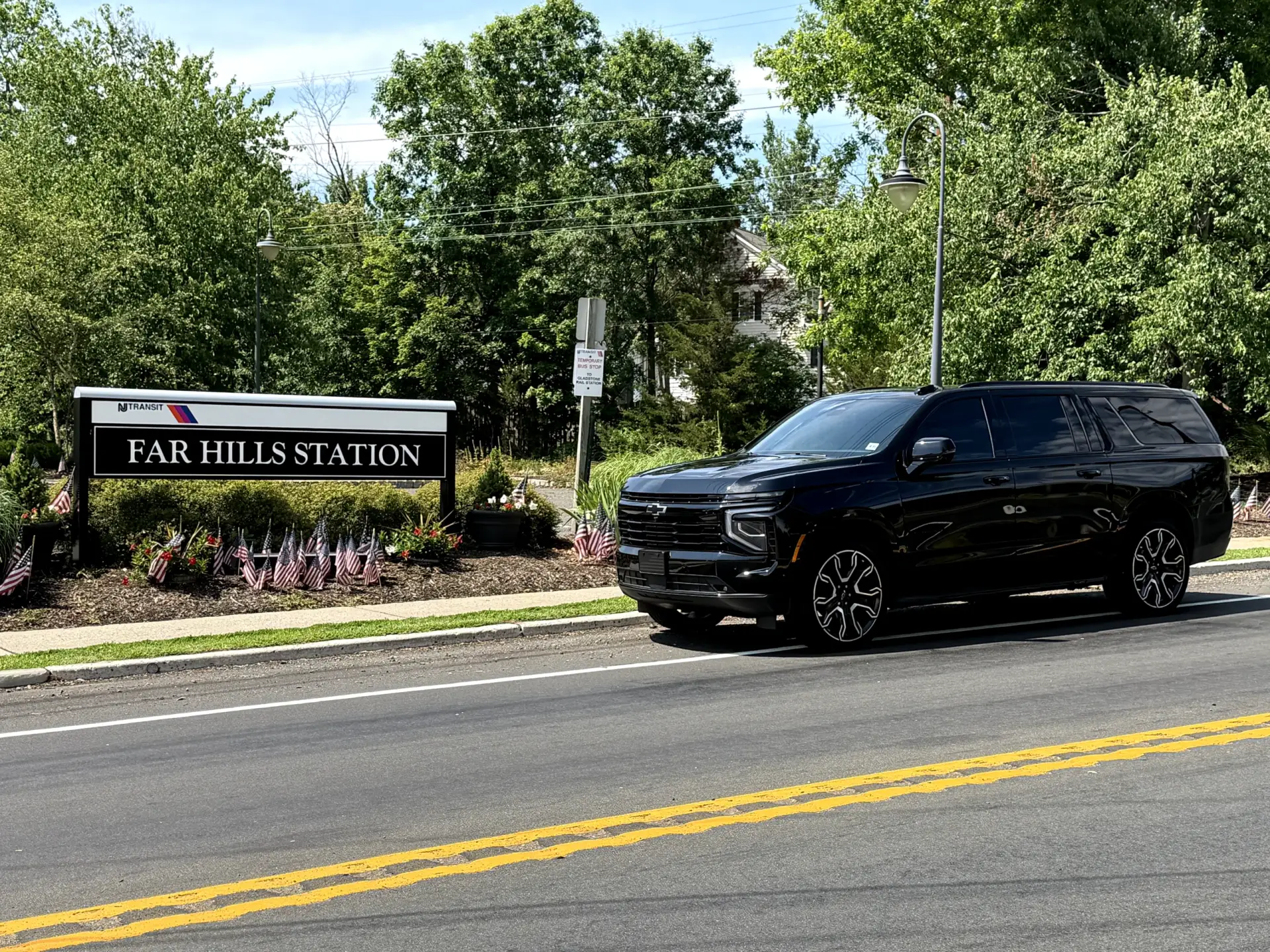 Black luxury SUV chauffeur service beside the Far Hills Station sign in Far Hills NJ
