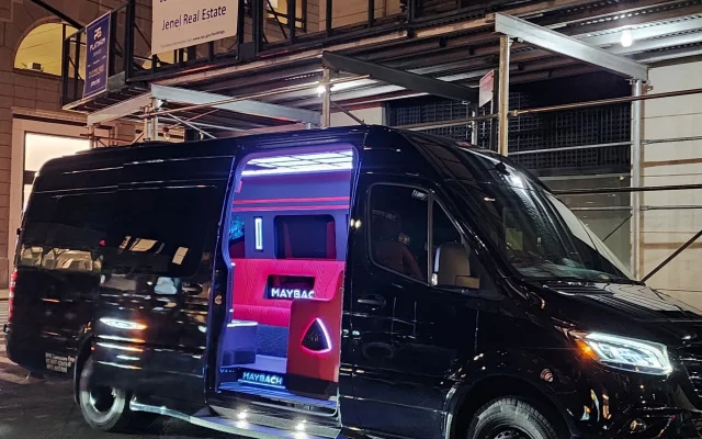 Black Mercedes-Benz Sprinter Maybach party bus parked on a Manhattan street at night with the side door open and pink cabin lighting visible