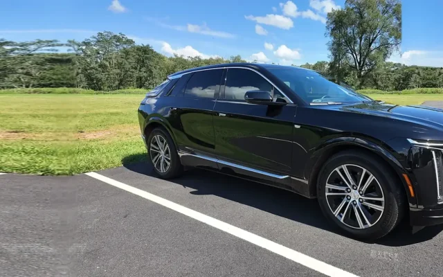 Black 2025 Cadillac LYRIQ EV parked on asphalt beside an open field, used for chauffeured electric car service by Basking Ridge Limousine Services in New Jersey