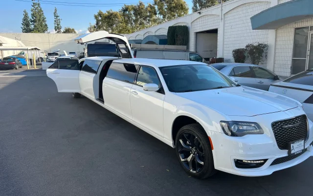 White Chrysler 300 stretch limousine with open doors parked outside a vehicle service center.