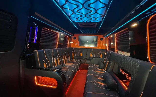 Wide-angle interior view of 2025 Mercedes Sprinter Maybach limo party bus with blue wave LED ceiling, custom orange accent leather seating, MAYBACH branding, and LCD screen — Basking Ridge Limousine NJ