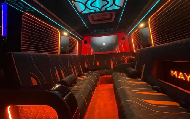 Full interior cabin of 2025 Mercedes Sprinter Maybach limo party bus at night showing teal wave LED ceiling, orange floor lighting, MAYBACH illuminated branding, flame-pattern leather seating and LCD screen — Basking Ridge Limousine NJ