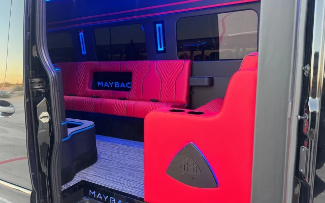 Open side door of the Maybach Sprinter party bus showing an illuminated Maybach sill plate, red quilted leather bench seating and blue LED ceiling lighting