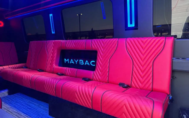 Close view of a red chevron-quilted leather bench in the Sprinter party bus, with seat belts along the cushion and a backlit Maybach panel set into the seat back